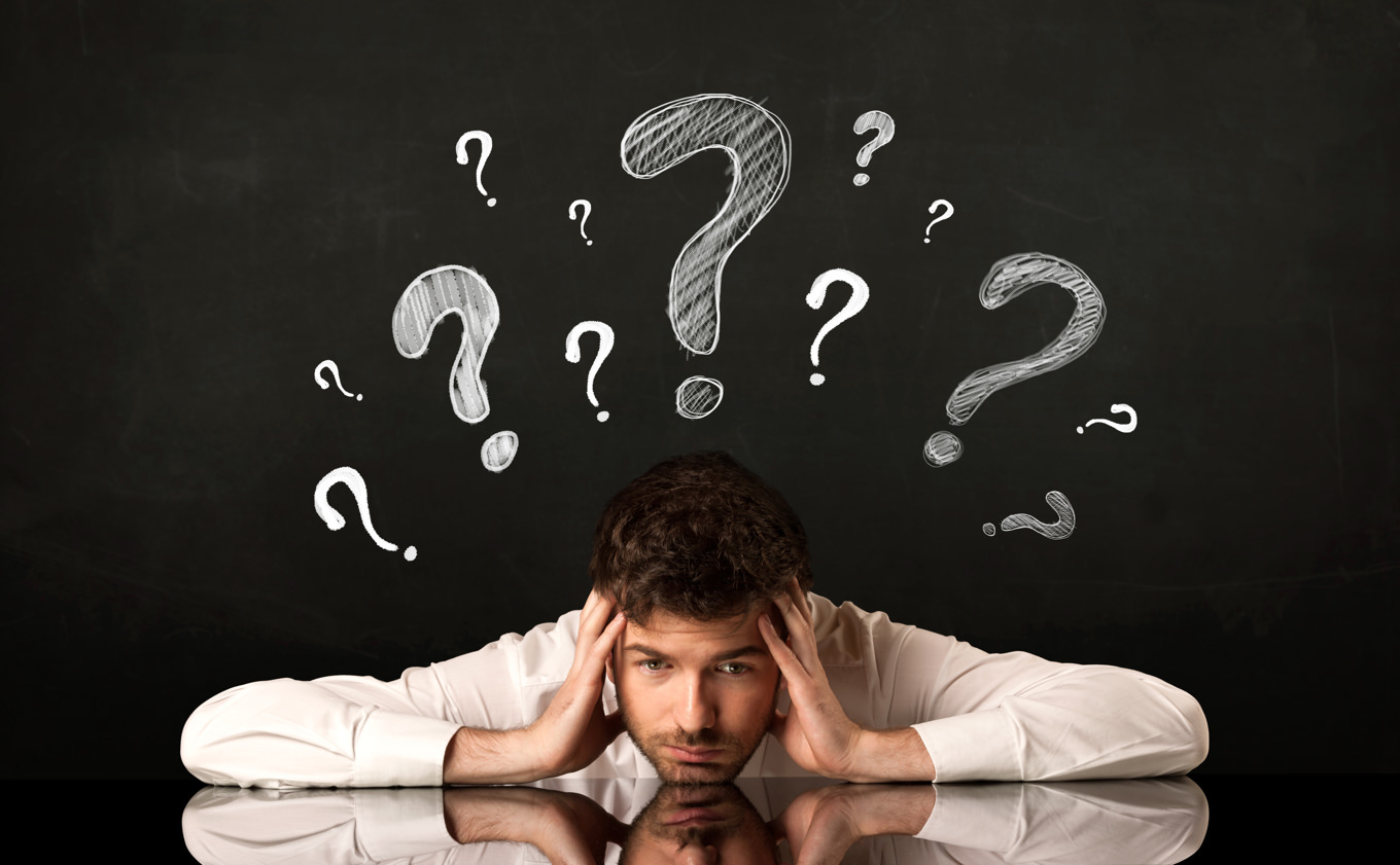 Depressed businessman sitting under question marks